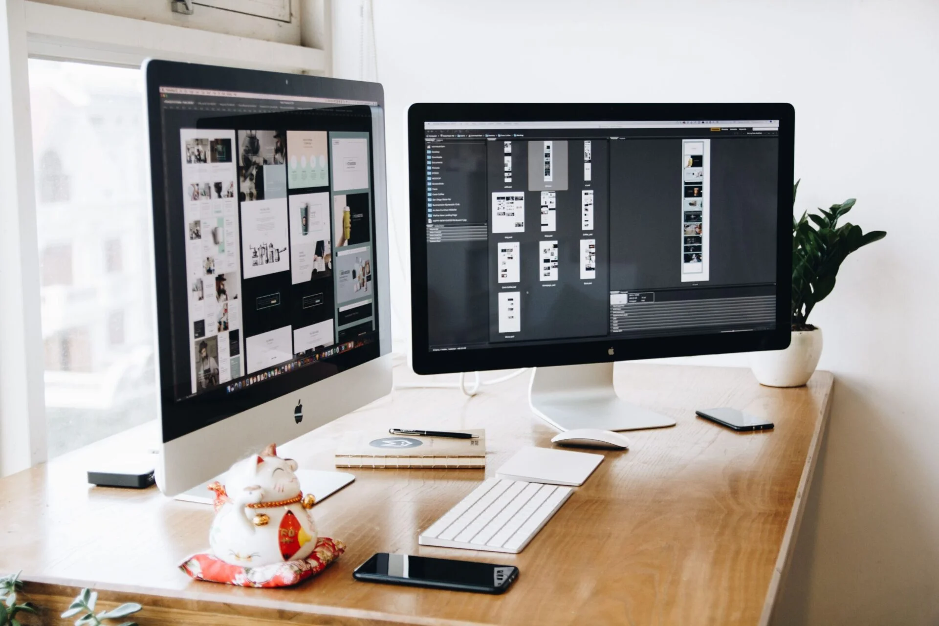 Two iMacs with keyboard and phones on a desk